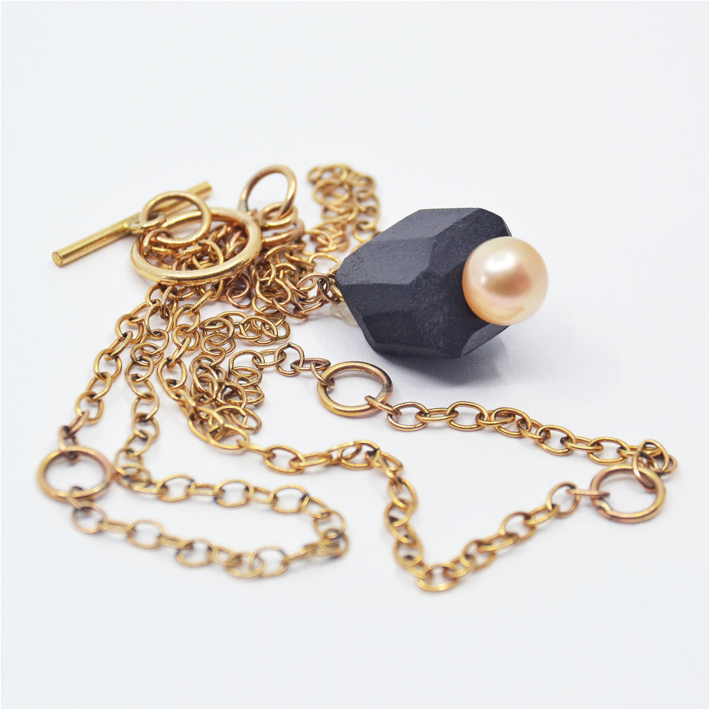 This charming necklace is handmade. The pendant consists of a handcrafted black porcelain bead, which is unglazed. The bead is adorned with a gorgeous peach colored pearl. The pendant is attached to a 14 karat gold-filled chain with toggle clasp.