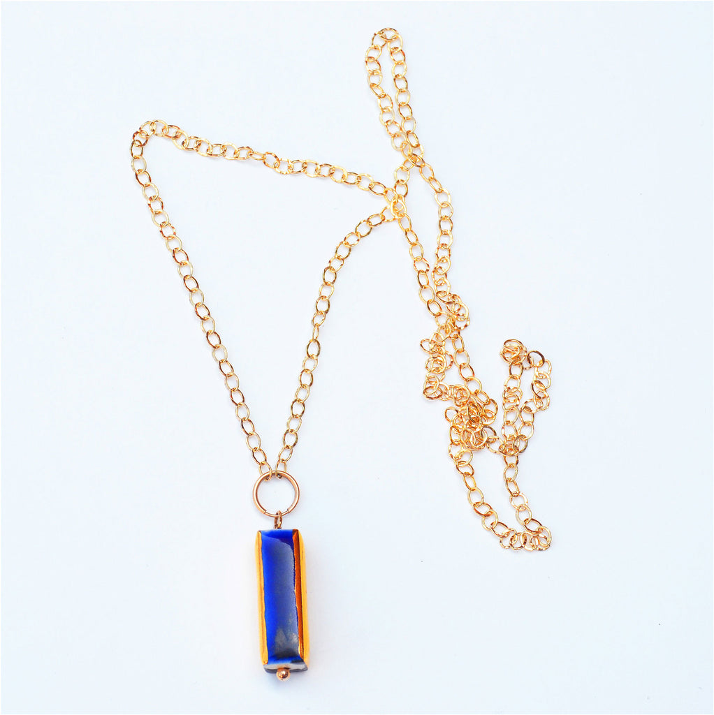 This stunning pendant necklace is hand-crafted of porcelain and glazed with glossy blue glaze and 22 karat gold. The pendant is attached to a 14 karat gold-filled ring and gorgeous long chain.