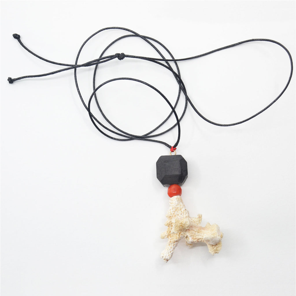 This unique pendant is made by hand. The porcelain bead is handcrafted and glazed with a matte black glaze. The pendant is adorned with a vintage carnelian bead and a white coral found on a beach of Long Island, NY. The pendant is attached to a 14 karat gold-filled ring and black adjustable jewelry cord.