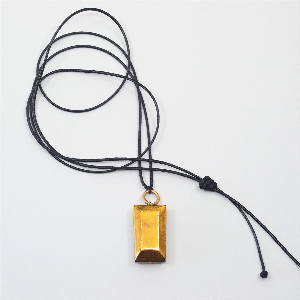 This beautiful pendant is made by hand of black porcelain. The pendant is glazed with 22 karat gold luster on one side, while the back is left unglazed to reveal the raw beauty of the black porcelain. The gold pendant is attached to a 14 karat gold-filled ring and adjustable black jewelry cord.
