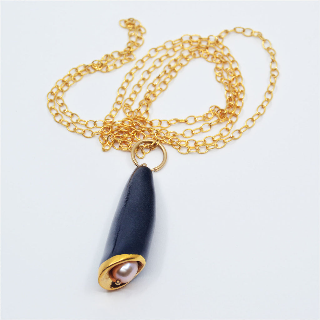 This beautiful unique pendant necklace is made of a handcrafted porcelain bead and pearl. The pendant is glazed with dark blue glaze and 22 karat gold luster. The pendant is attached to a 14 karat gold-filled ring and long chain.