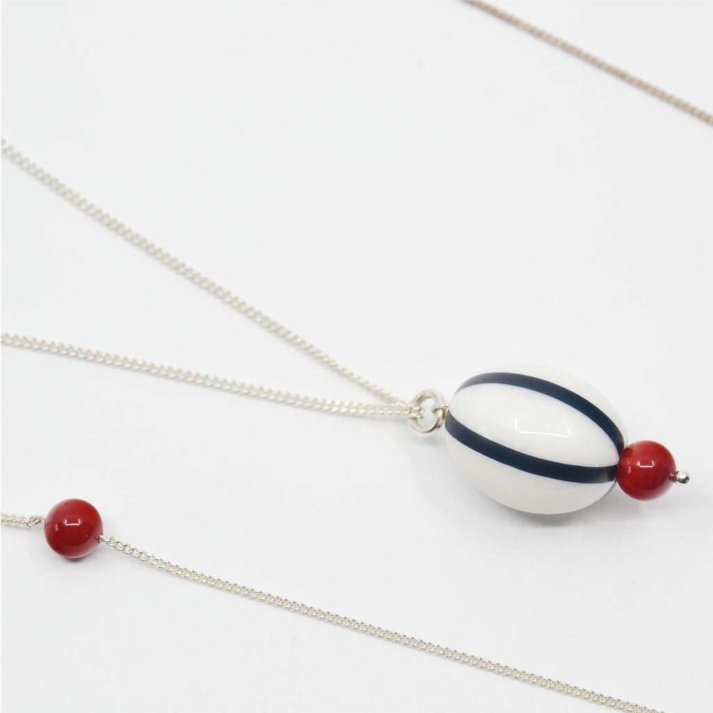 This unique necklace is made by hand. The necklace is adorned with an oval shaped white porcelain bead with black stripes, and vintage glass beads in coral color. The porcelain bead is attached to a sterling silver ring and a long fine sterling silver chain.