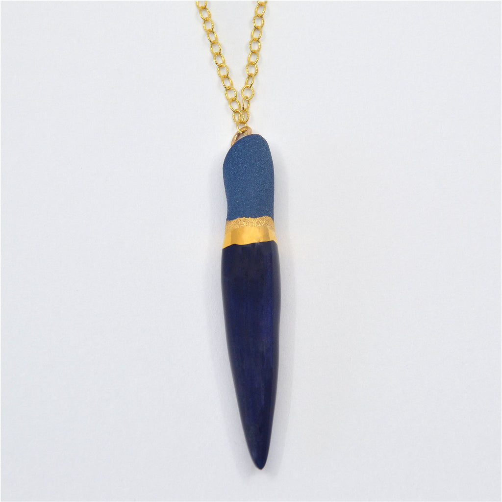 This pretty pendant necklace is made by hand. The pendant is handcrafted of blue porcelain, the top of the pendant is unglazed, while the bottom part is glazed with smooth navy blue glaze, and a stripe of 22 karat gold luster where the glazed and unglazed surfaces meet. The pendant is attached to a 14 karat gold-filled chain and magnetic clasp.