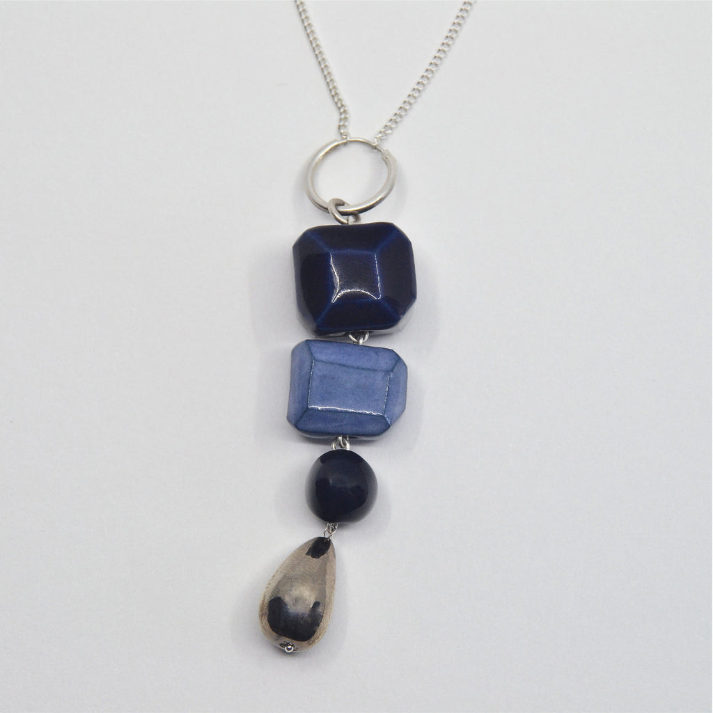This gorgeous dangle pendant necklace is handmade. The pendant is hand-crafted of porcelain beads in shades of blue and a drop shaped bead glazed in white gold. The Pendant is attached to a sterling silver ring and fine chain with clasp.