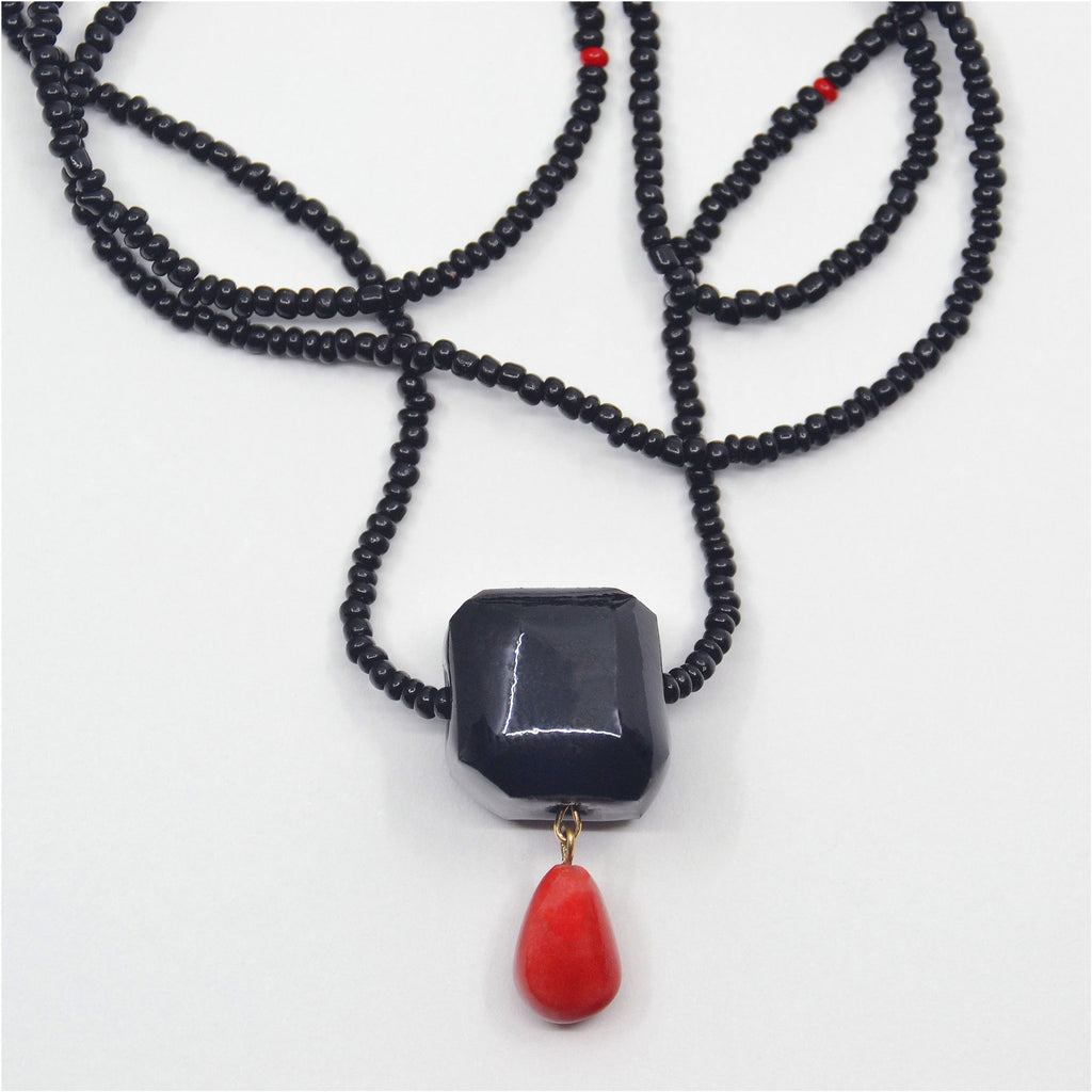 This gorgeous unique necklace is handmade. The long chain is mad of small vintage glass beads in black color, with a few red mixed in. The centerpiece of this necklace is a hand-faceted porcelain bead, glazed in glossy black with a drop shaped handcrafted porcelain bead dangle, glazed in deep red color. 
