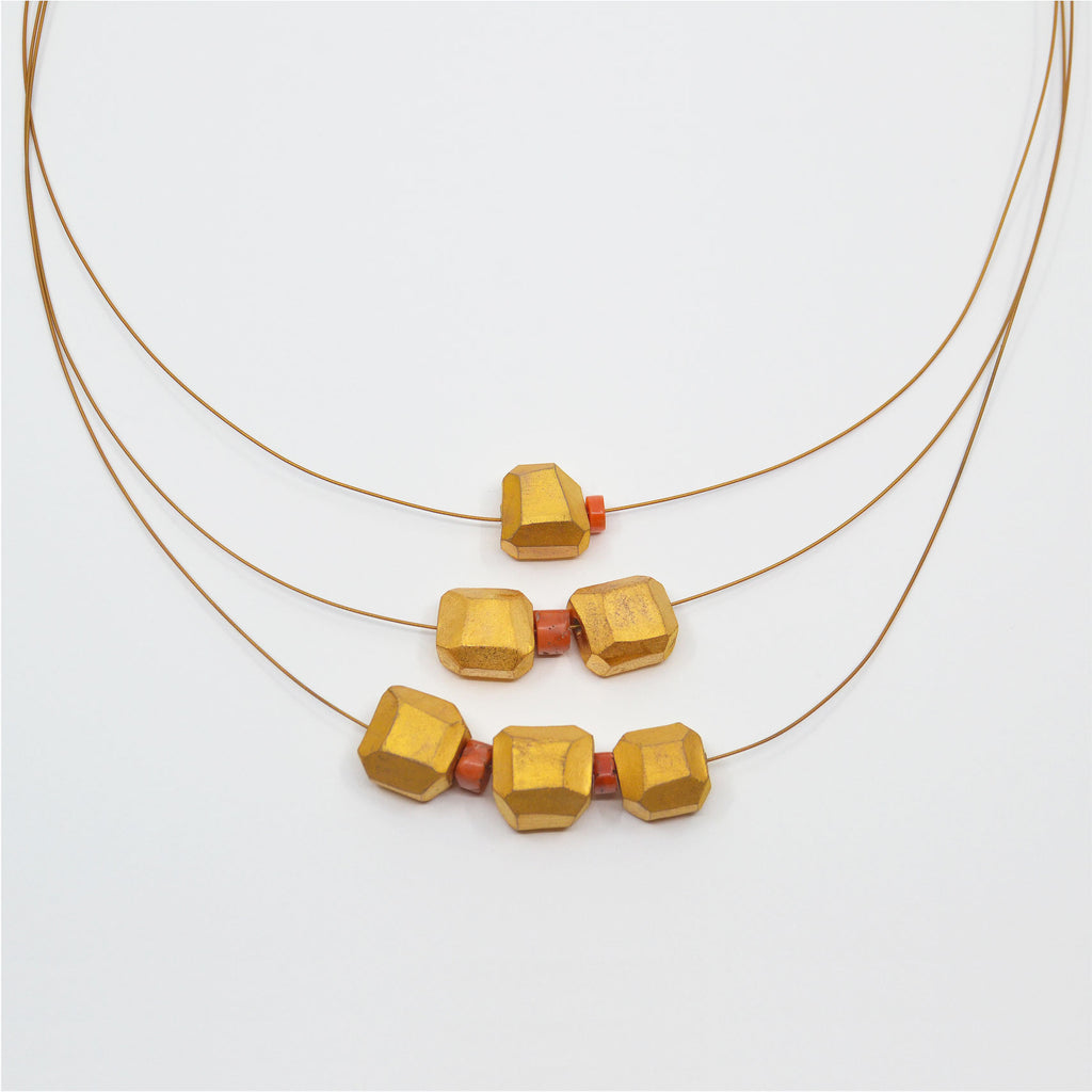This striking three tier necklace consists of handcrafted and gold glazed porcelain beads, as well as vintage coral. The corals and porcelain beads are strung on three layers of golden jewelry cord. The clasp is a 14 karat gold-filled magnetic clasp.