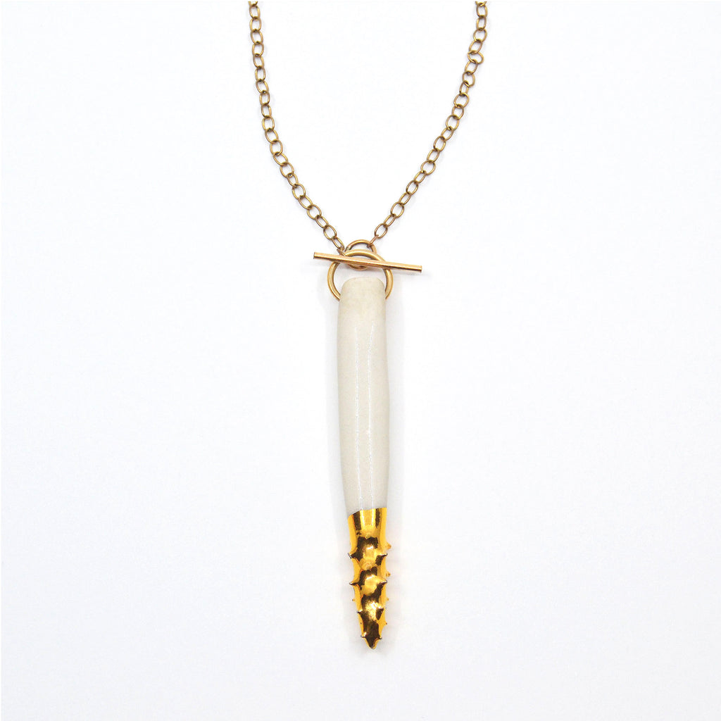 This unique pendant necklace is handmade. The pendant is hand-crafted of white porcelain, the pointy spiked tip is glazed with 22 karat gold. The pendant is attached to a 14 karat gold-filled chain and toggle clasp. The toggle opens in the front just above the pendant.  