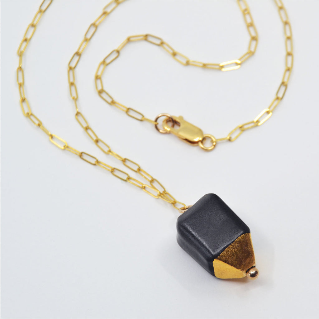This pretty porcelain pendant necklace is made by hand. The bead is glazed matte black and the dome shaped tip is glazed with 22 karat gold luster. The pendant is attached to a 14 karat gold-filled chain and clasp.