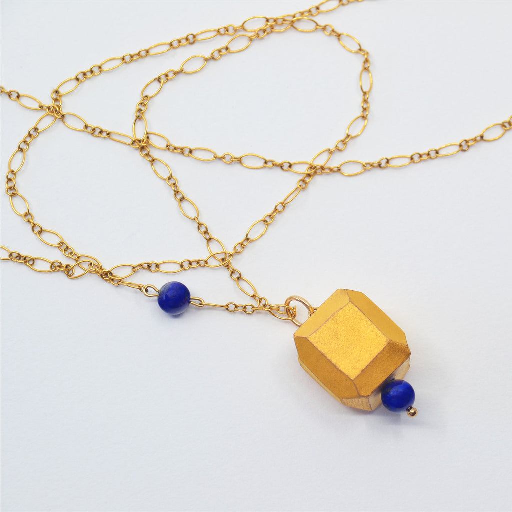 This pretty necklace is made by hand. The pendant is made of a hand-faceted porcelain bead, glazed with matte 22 karat gold, and a lapis lazuli bead. The pendant is attached to a 14 karat gold-filled ring and chain with clasp. There is a lapis lazuli bead strung on the golden chain. 