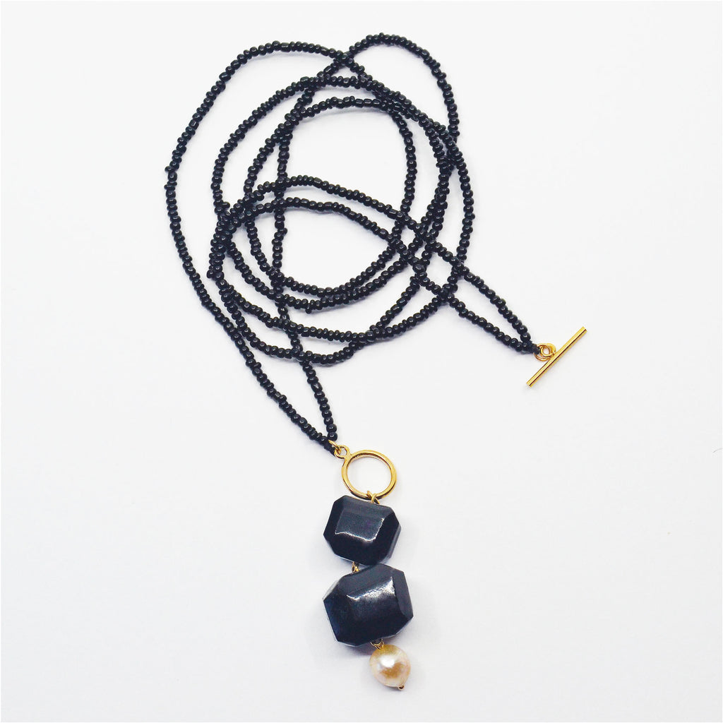 This unique pendant necklace is made by hand, the porcelain beads are hand-faceted and glazed in a glossy black. The pendant is adorned with a gorgeous vintage pearl. The dangle pendant is attached to a 14 karat gold-filled ring and a handmade chain consisting of black vintage glass beads. The necklace can be worn long or doubled up and worn as a choker by closing the 14 karat gold-filled toggle clasp in the front just above the pendant.