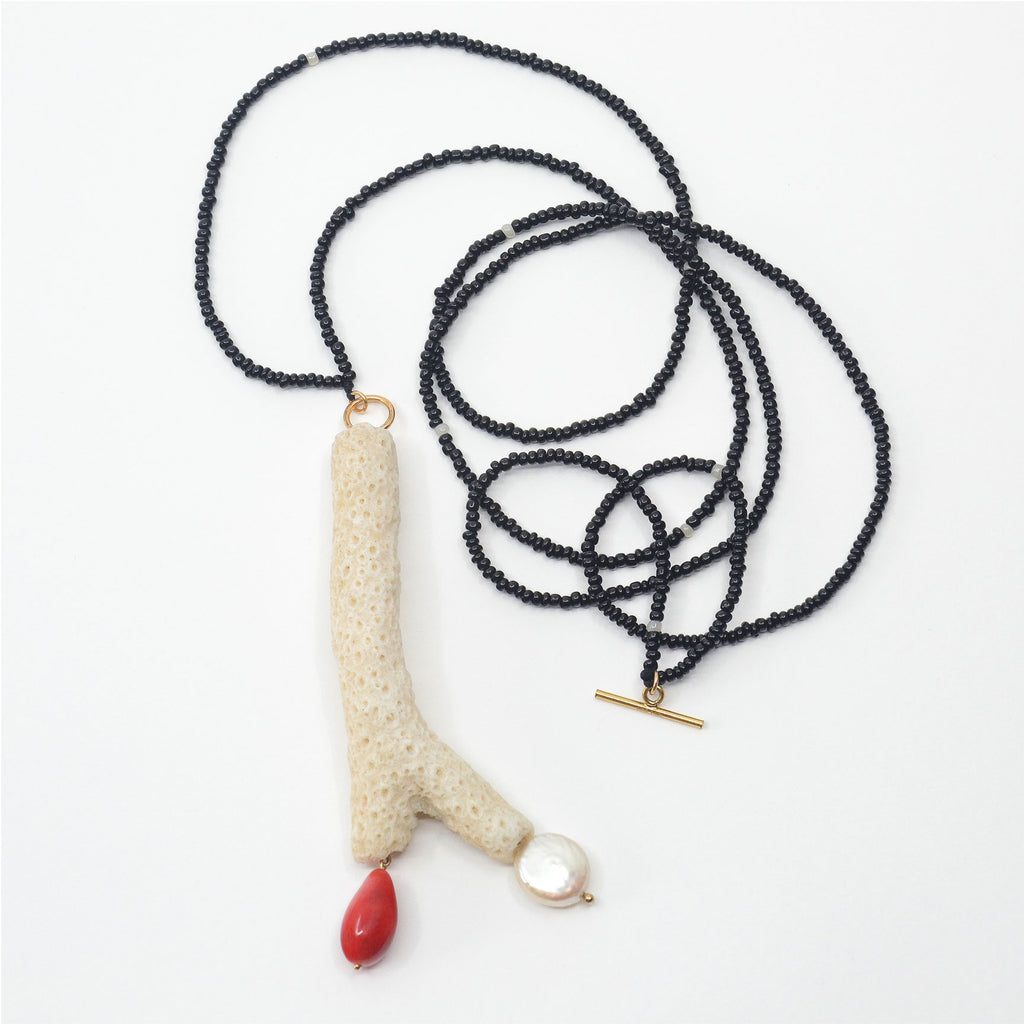 This gorgeous pendant necklace is made by hand. The white coral branch was found on a beach of Long Island, NY. The red drop shaped porcelain dangle bead is glazed in red . The pearl is vintage in silver-pink hue. The chain is made of vintage glass beads in black color with a few white glass beads sprinkled in-between. The toggle clasp is 14 karat gold-filled and opens in the front just above the pendant. The necklace can also be worn long. 