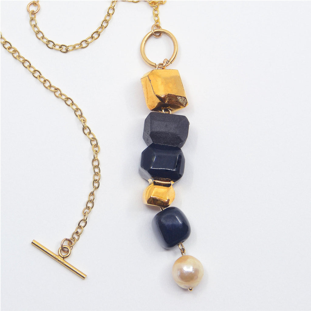 This beautiful dangle necklace is made by hand. The dangle pendant is made of handcrafted  porcelain beads, they are glazed in darkest blue and 22 karat gold, and partially left unglazed, creating a striking contrast, especially with a beautiful vintage dangling pearl dangling at the bottom tip. The dangle pendant is attached to a 14 karat gold-filled ring and chain with a toggle clasp that opens in the front.