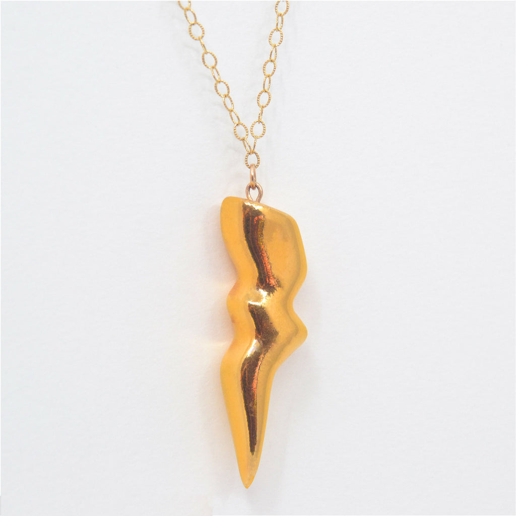 This unique pendant is handmade of porcelain in the shape of a thunderbolt. The thunderbolt is glazed with 22 karat gold, and is attached to a 14 karat gold-filled chain with clasp.