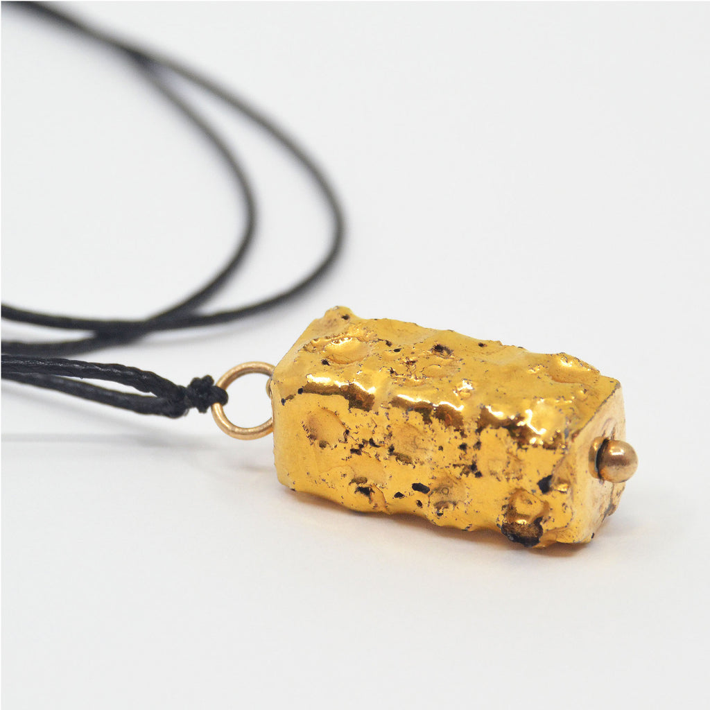 This stunning porcelain pendant is handmade of porcelain. The porcelain bead is glazed with 22 karat gold and the texture is made by hand. The pendant is attached to a 14 karat gold-filled ring and adjustable black jewelry cord.