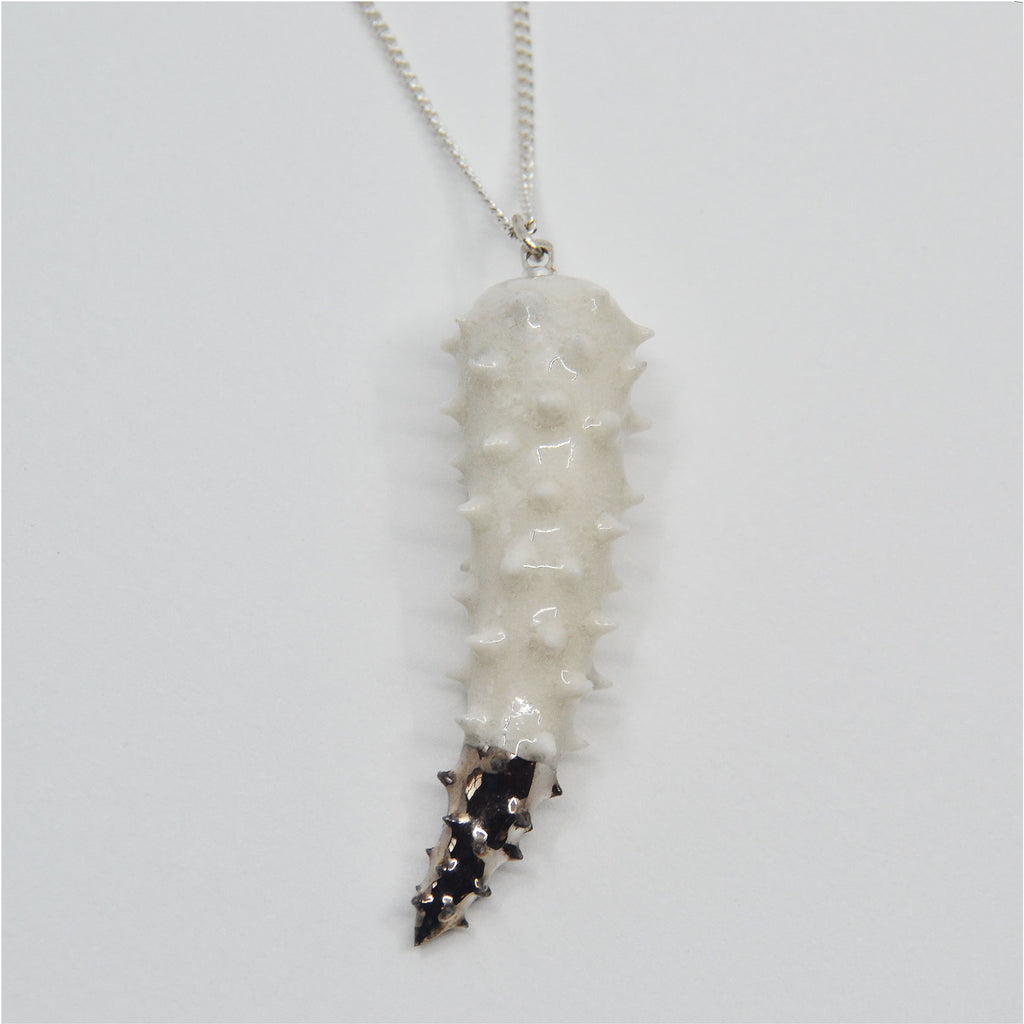 This unique pendant necklace is handmade. The pendant is crafted in the shape of a tiger tooth, the spikes are applied individually by hand. The pendant is glazed white, with a tip glazed in white gold. The pendant is attached to a fine sterling silver chain and clasp.
