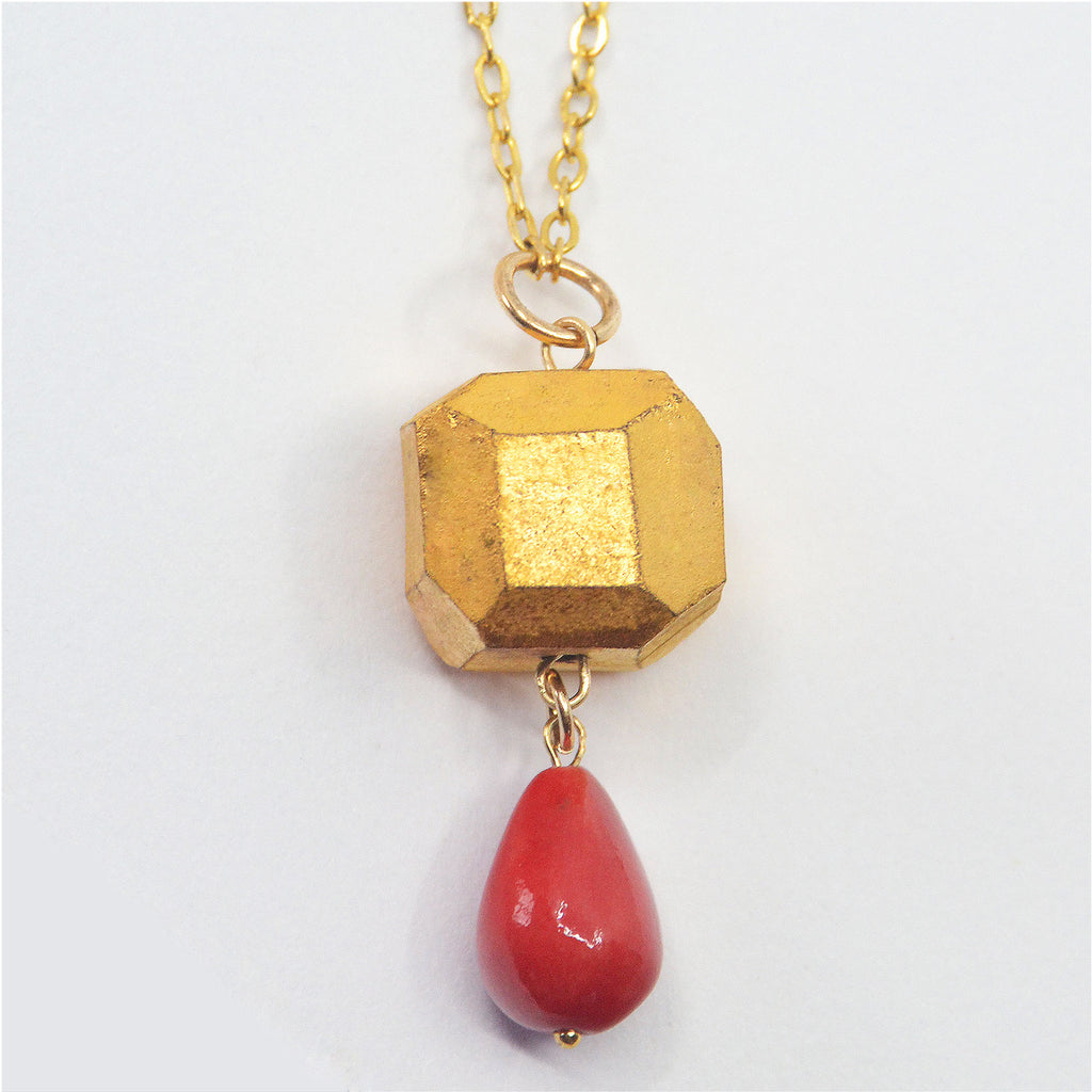 This beautiful unique pendant necklace is handmade. The bead is crafted of porcelain and hand-faceted, it is glazed with 22 karat gold and adorned with a drop shaped porcelain bead glazed in deep red. The pendant is attached to a 14 karat gold-filled ring and long chain.