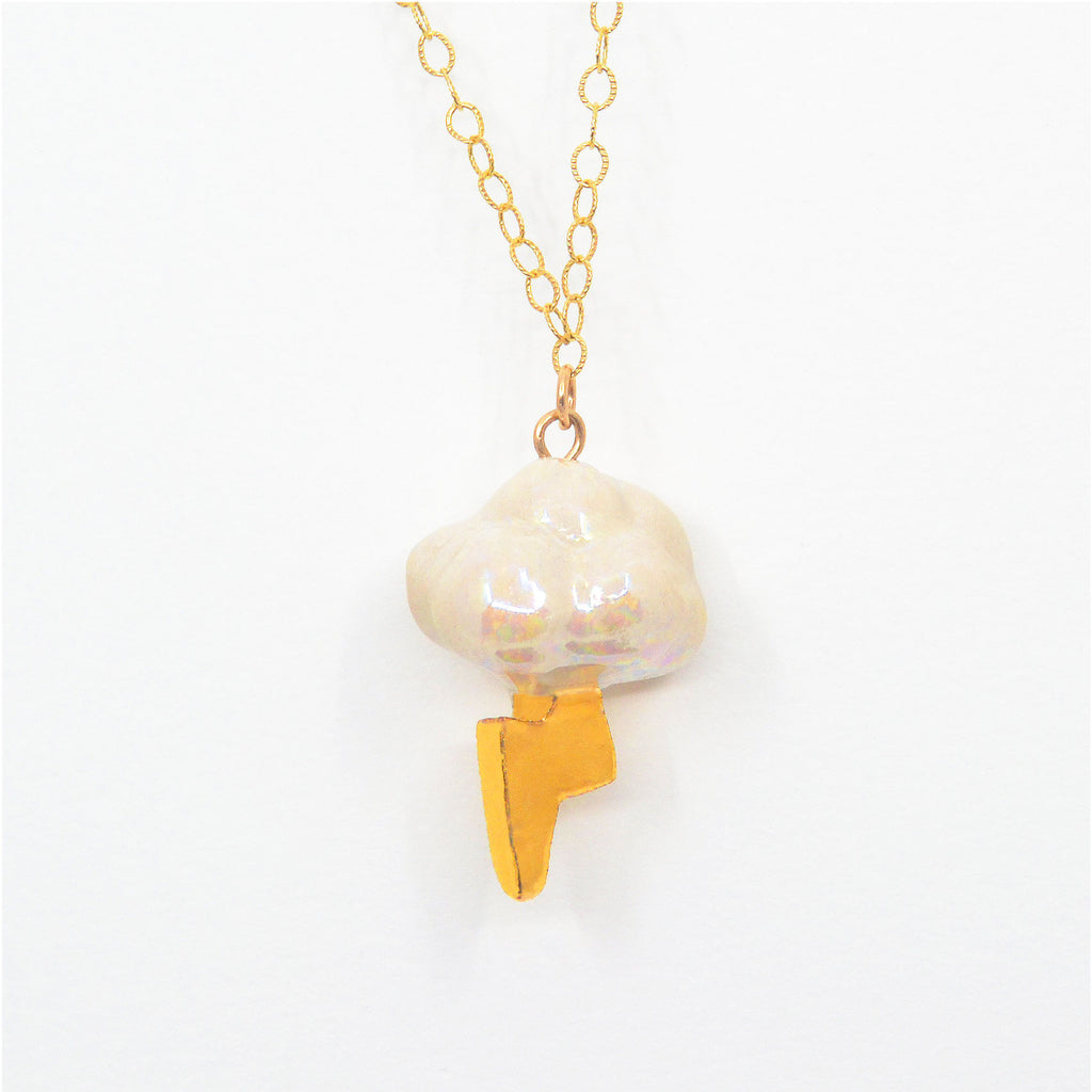 This unique pendant is handcrafted of porcelain. The cloud shape is glazed in glossy mother of pearl glaze, and the lightning bolt is glazed with 22 karat gold. The pendant is attached to a 14 karat gold-filled chain with clasp.