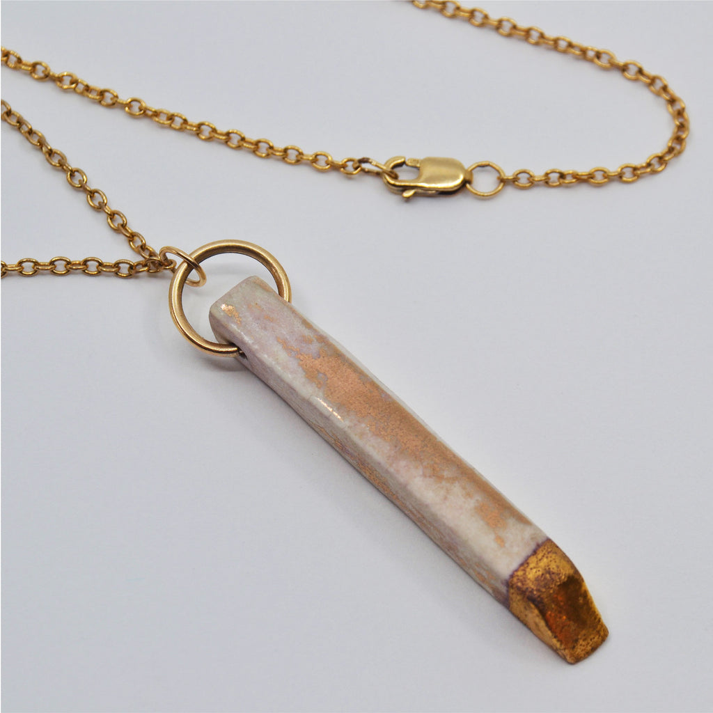This unique pendant necklace is handcrafted and consists of a porcelain pendant wich is partially glazed with a matte 22 karat glaze in patina effect. The pendant is attached to a 14 karat gold -filled chain and clasp.
