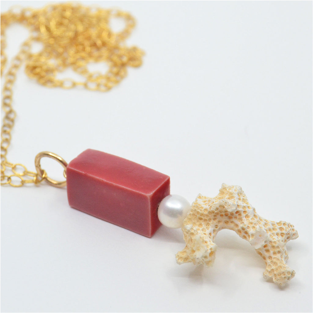 This unique Pendant is handmade. The porcelain bead is handcrafted and glazed red, the pendant is adorned with a vintage white pearl and a white coral found on a beach of Long Island, New York. The pendant is attached to a 14 karat gold-filled ring and long chain.